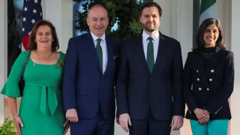 Reuters U.S. Vice President JD Vance, second lady Usha Vance, Micheal Martin and his wife Mary O'Shea posing in line and smiling at the camera.