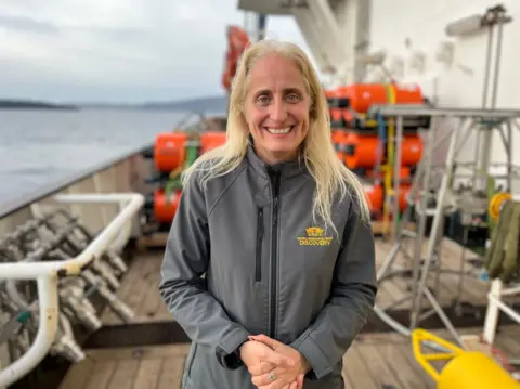 Tom Ingham/BBC A photograph of Professor Evi Nomikou on deck of the RRS Discovery with red and yellow equipment around her