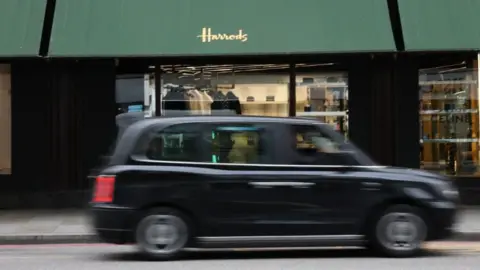 Reuters A blurry black cab rushes past the Harrods shop front, with green awnings with "Harrods" printed in gold on one.